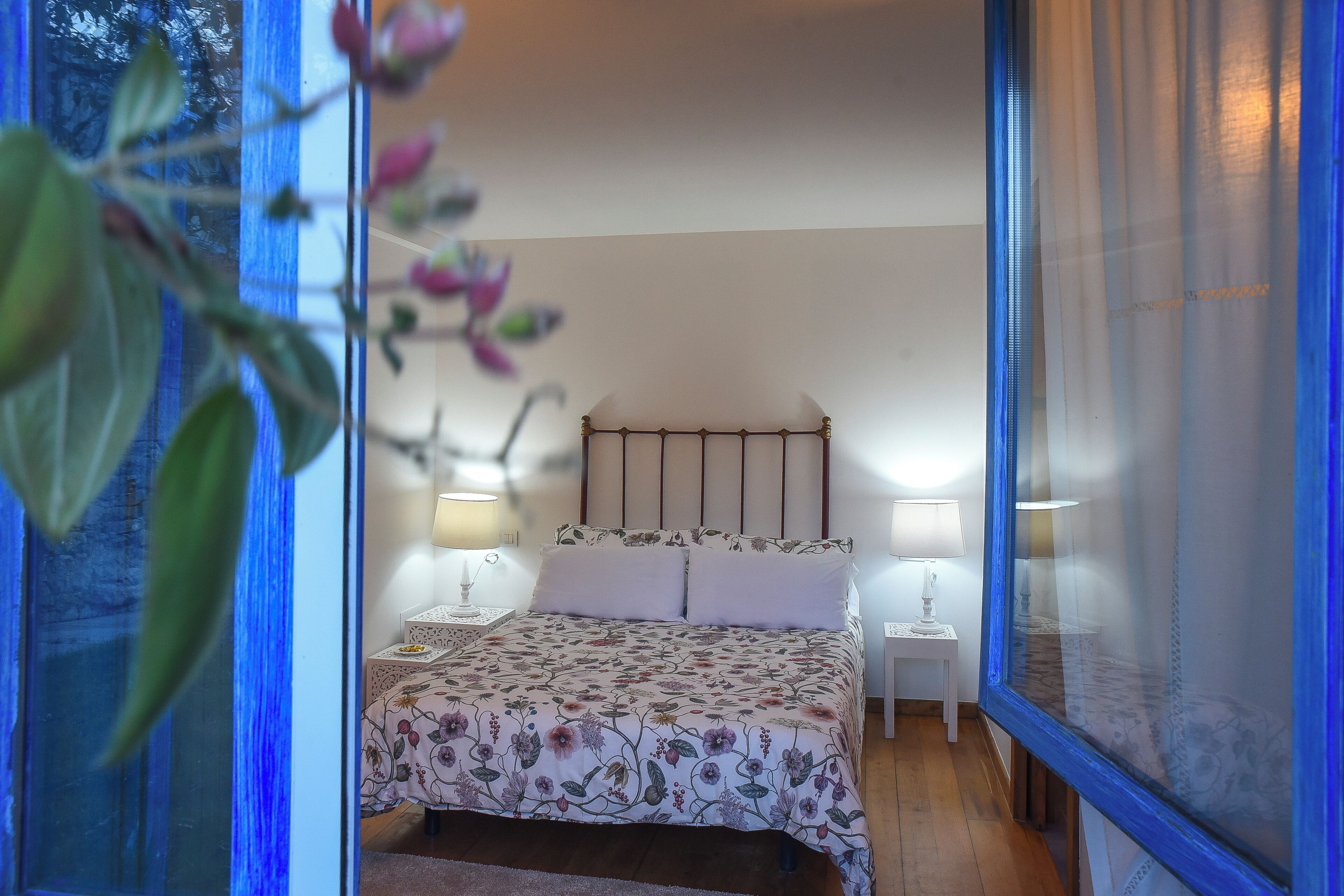Une chambre à coucher avec un lit, deux tables de chevet et une fenêtre donnant sur un paysage verdoyant.