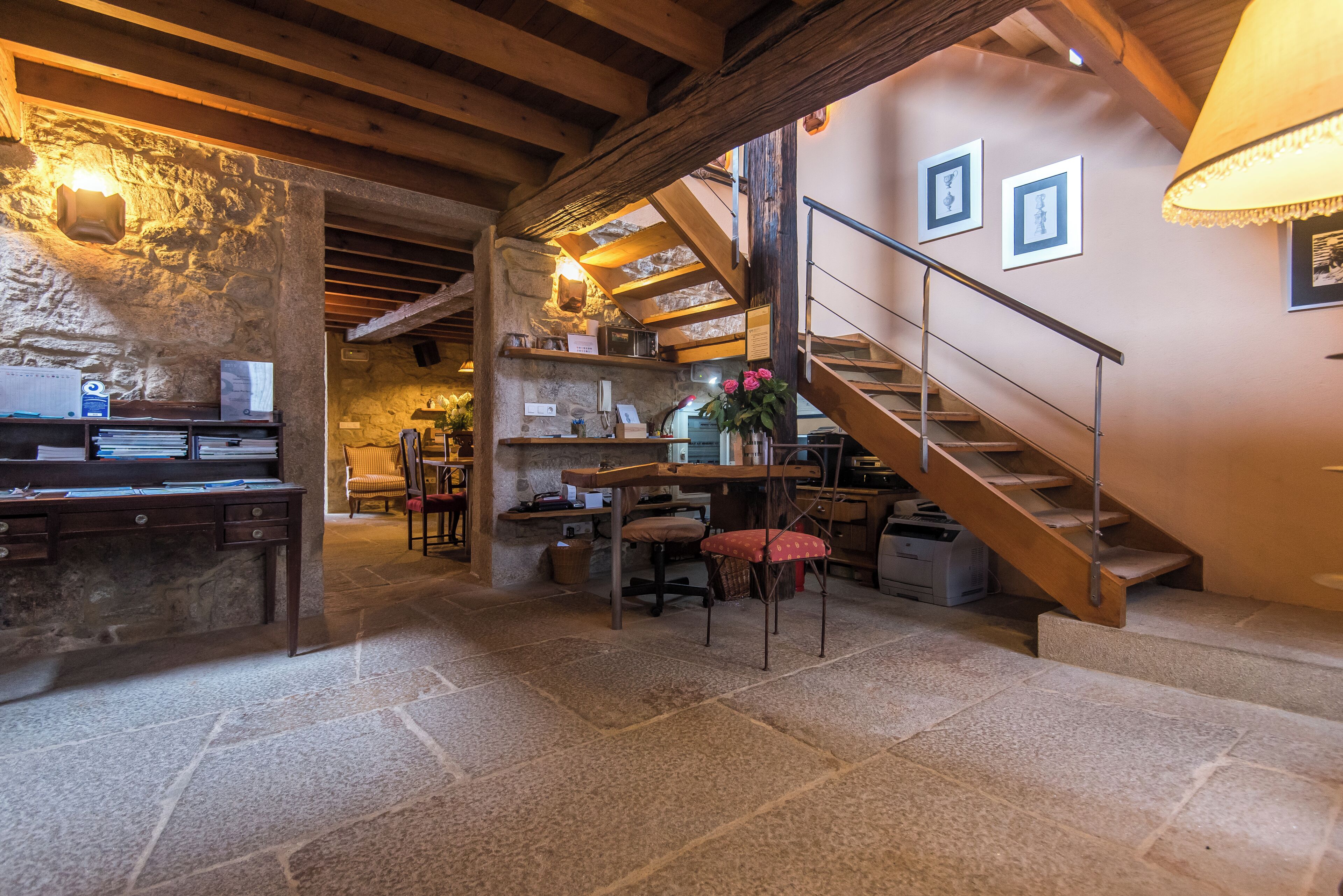A rustic interior with a stone wall, wooden beams, a staircase, and a desk with various items.