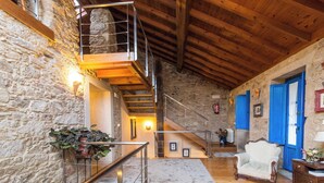 Un interior rústico con pared de piedra, escalera de madera y un sillón blanco.