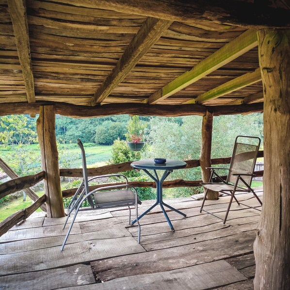 A wooden deck with a table and chairs, overlooking a lush green landscape.