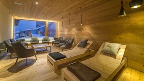 Un intérieur chaleureux en bois, avec un canapé, des fauteuils et une grande fenêtre donnant sur un paysage enneigé.
