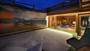 Un espace extérieur moderne, avec un sol enneigé, un fauteuil de relaxation et une vue sur un paysage montagneux, visible à travers une grande fenêtre.
