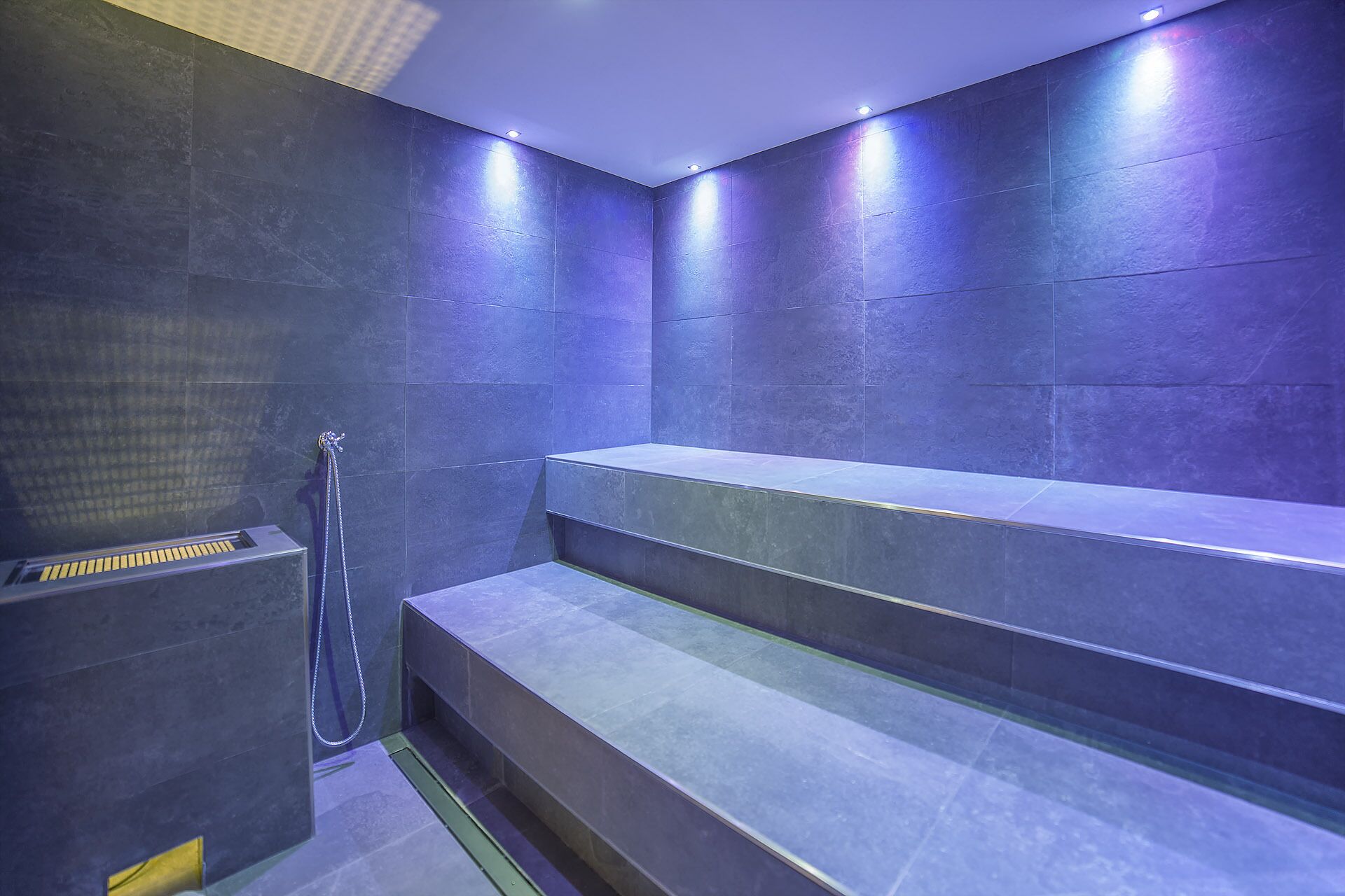 Un baño moderno con baldosas azul oscuro, un banco empotrado y una zona de ducha.