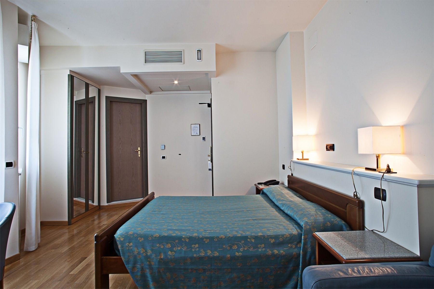 Une chambre d’hôtel comprenant un lit, une table de chevet, une lampe et une porte donnant sur une autre pièce.