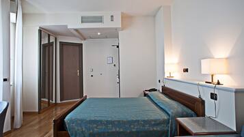 Une chambre d’hôtel comprenant un lit, une table de chevet, une lampe et une porte donnant sur une autre pièce.