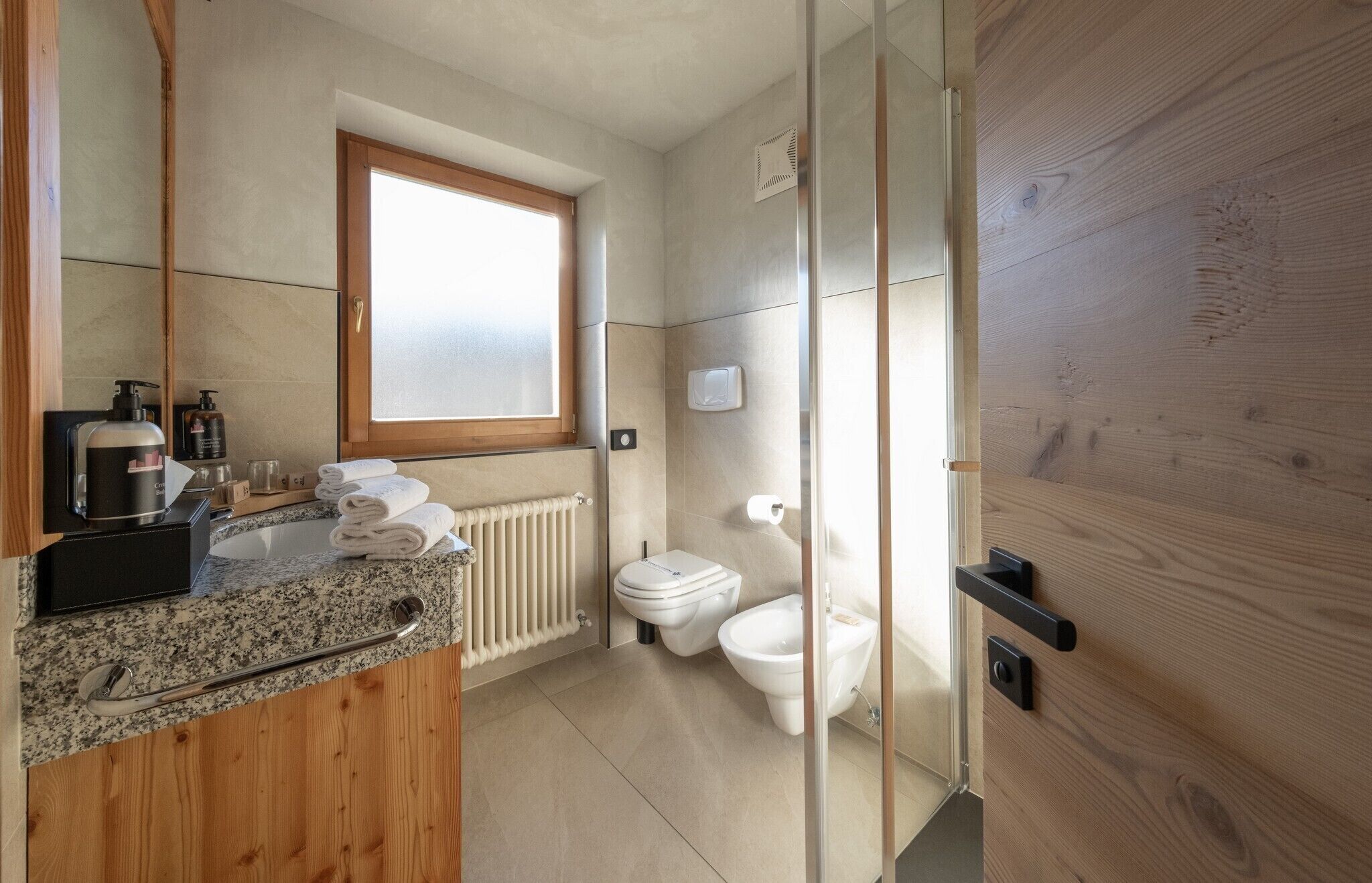 A modern bathroom with a granite countertop, a wooden vanity, a toilet, and a bidet.