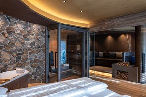 A modern bedroom with a stone wall, a glass door leading to a balcony, a wooden floor, and a built-in fireplace.