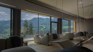 A modern room with large windows, a hammock, and a view of mountains. - La Roccia Wellness Hotel (Cavalese)
