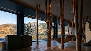 A spacious room with a large window offering a mountain view, wooden beams, and a modern sofa. - La Roccia Wellness Hotel (Cavalese)