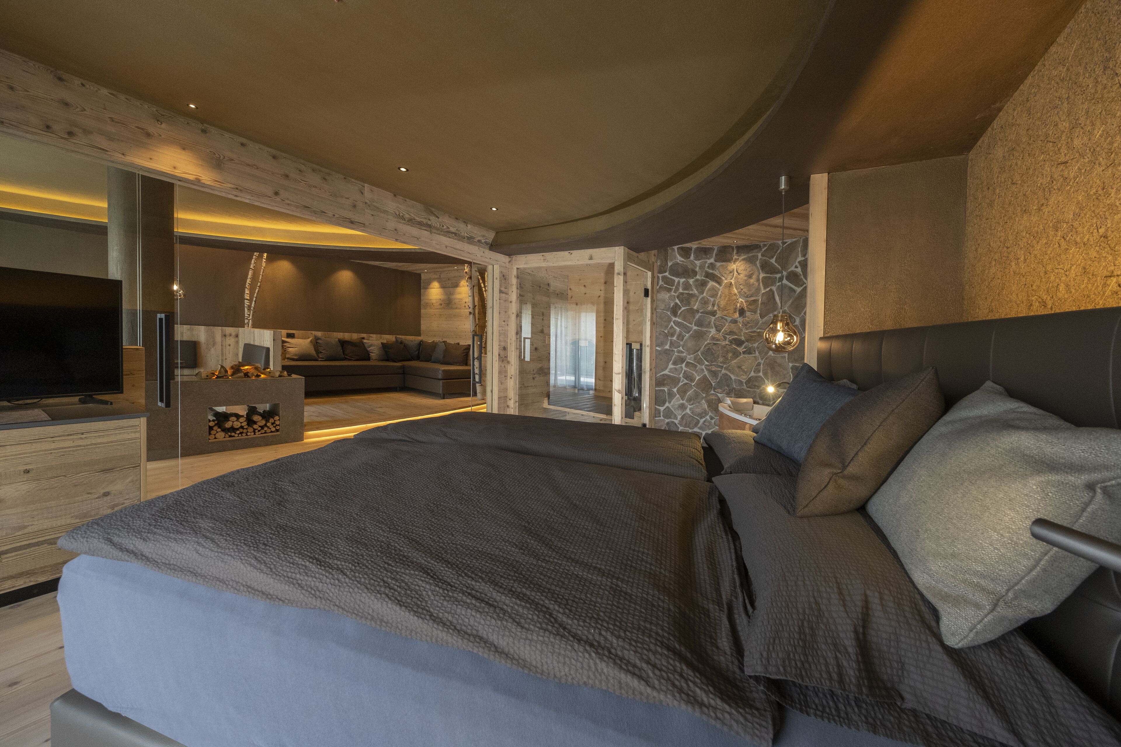 A modern bedroom with a large bed, a built-in TV, and a cozy seating area.