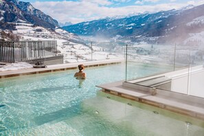 A person in a clear pool with a view of snow-covered mountains.