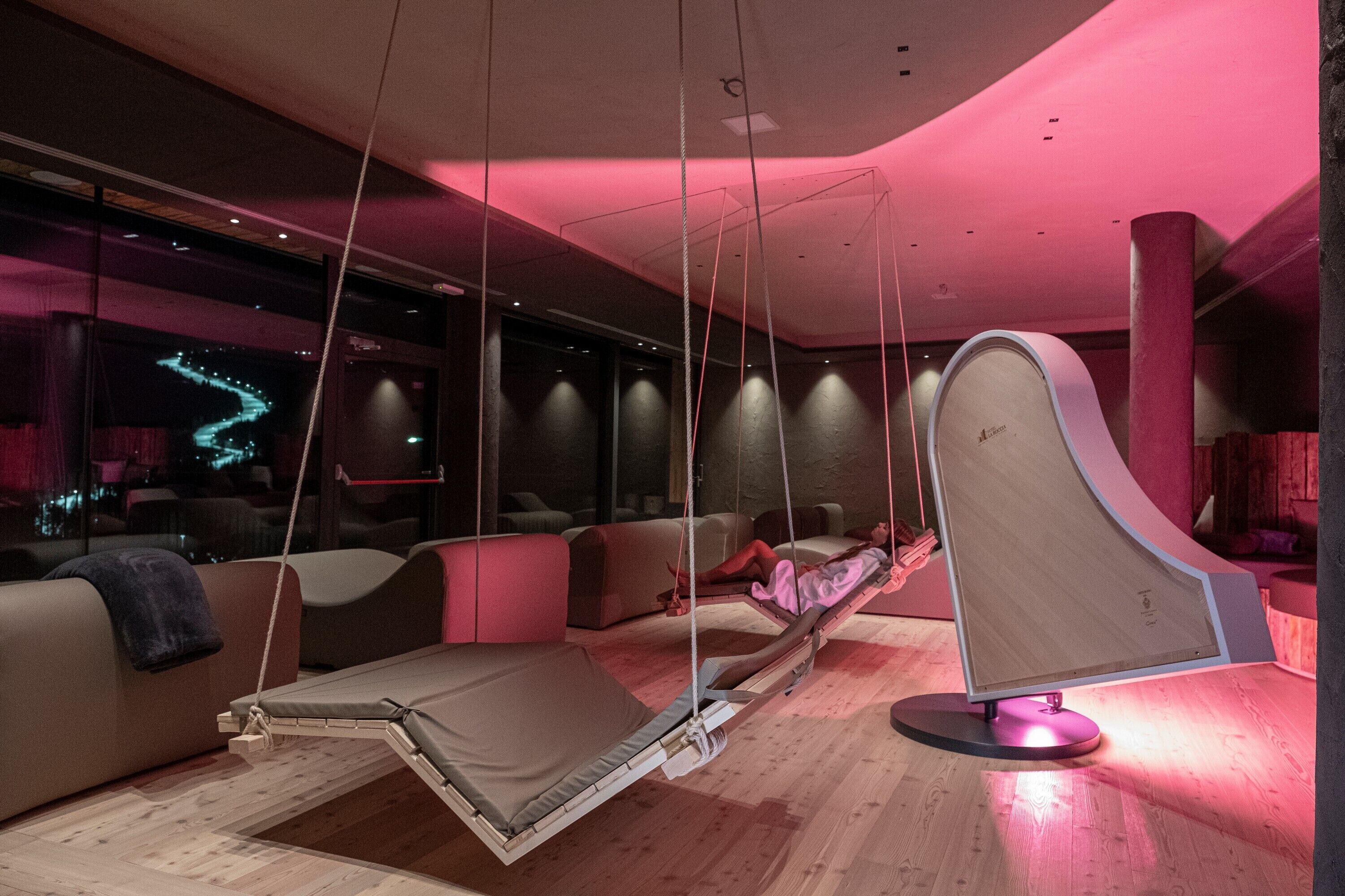 Un espace de détente moderne avec un fauteuil suspendu, des sièges confortables et une vue sur le paysage urbain illuminé la nuit.