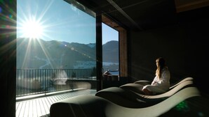 A person sitting on a curved bench on a balcony with a view of mountains and a body of water. - La Roccia Wellness Hotel (Cavalese)