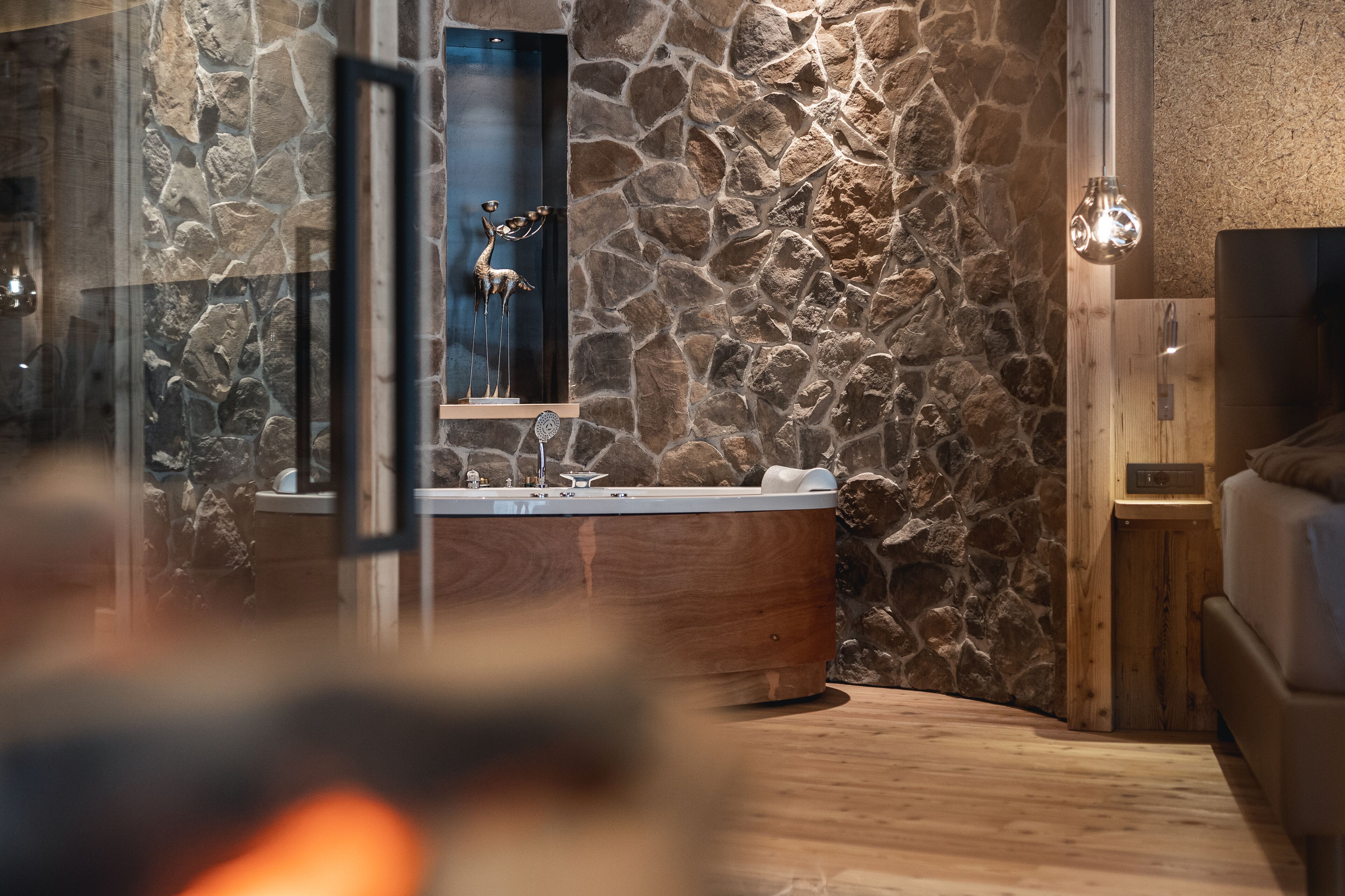 Un baño moderno con pared de piedra, una bañera independiente y suelo de madera.