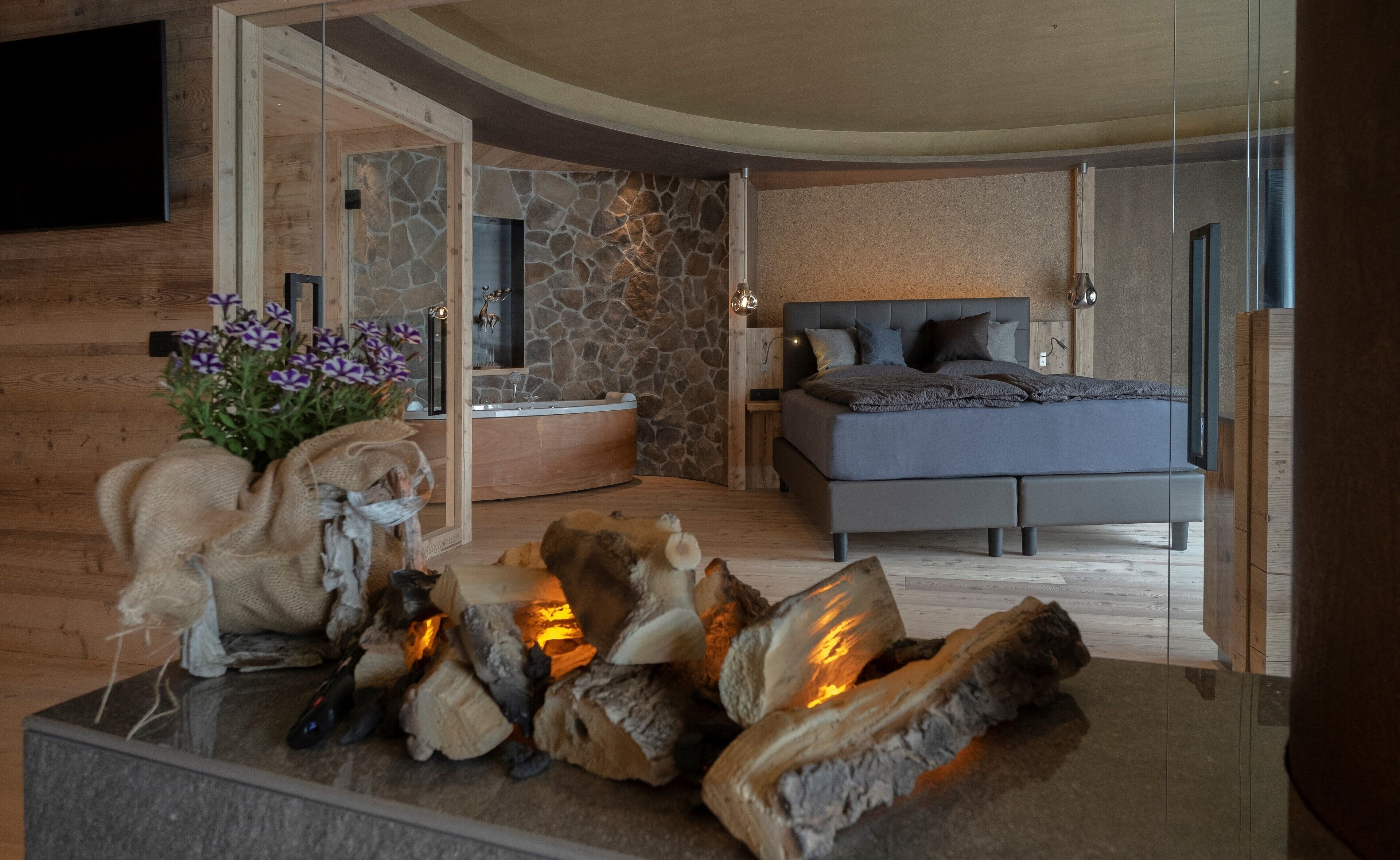 Une chambre moderne avec un mur en pierre, un lit, une cheminée et un plancher en bois.