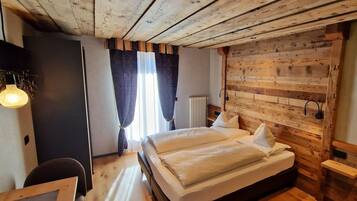 A cozy room with a wooden ceiling, a bed with white linens, a desk with a chair, and a window with curtains.