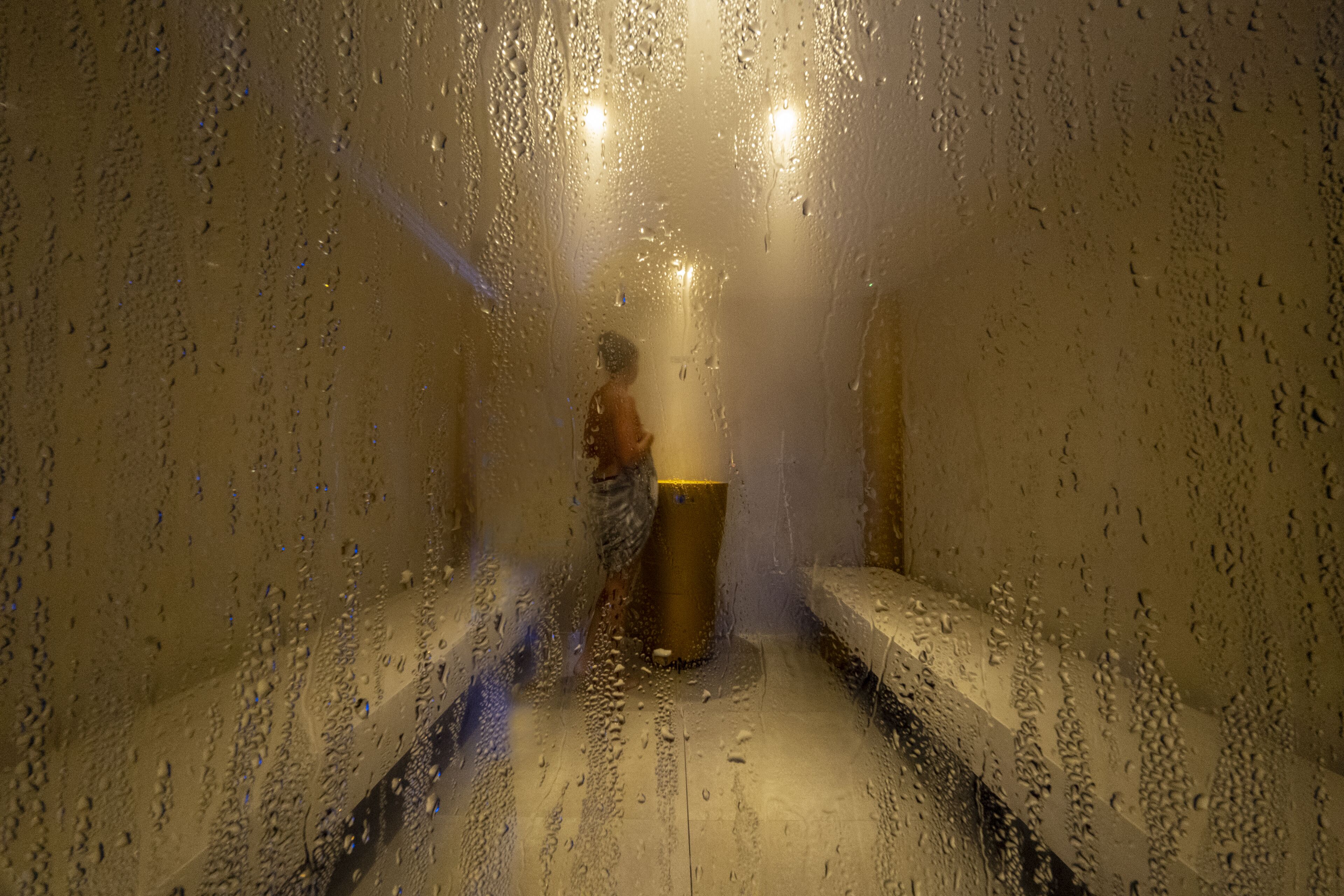 A narrow, wet corridor with benches on either side and a central pillar.