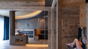 A modern interior with a wooden floor, a fireplace, and a seating area with a person. - La Roccia Wellness Hotel (Cavalese)