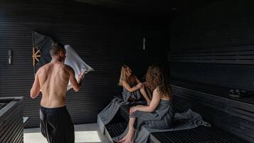 A sauna room with wooden benches and a person carrying a towel.