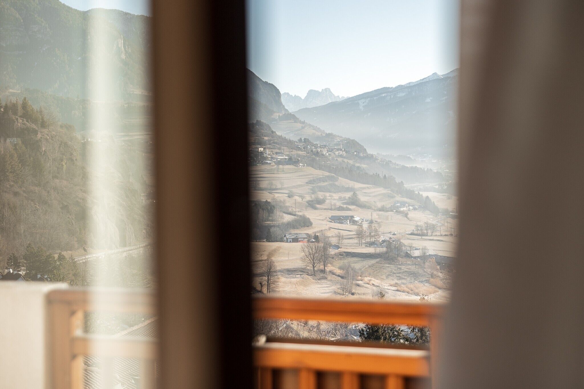 Une vue depuis une fenêtre donnant sur une vallée, avec des montagnes en arrière-plan.