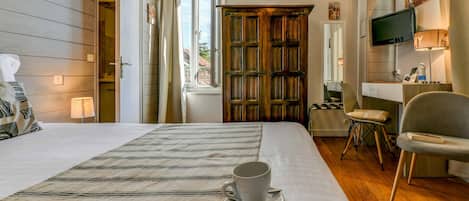 A hotel room with a bed, a desk with a lamp, a television, and a window with curtains.