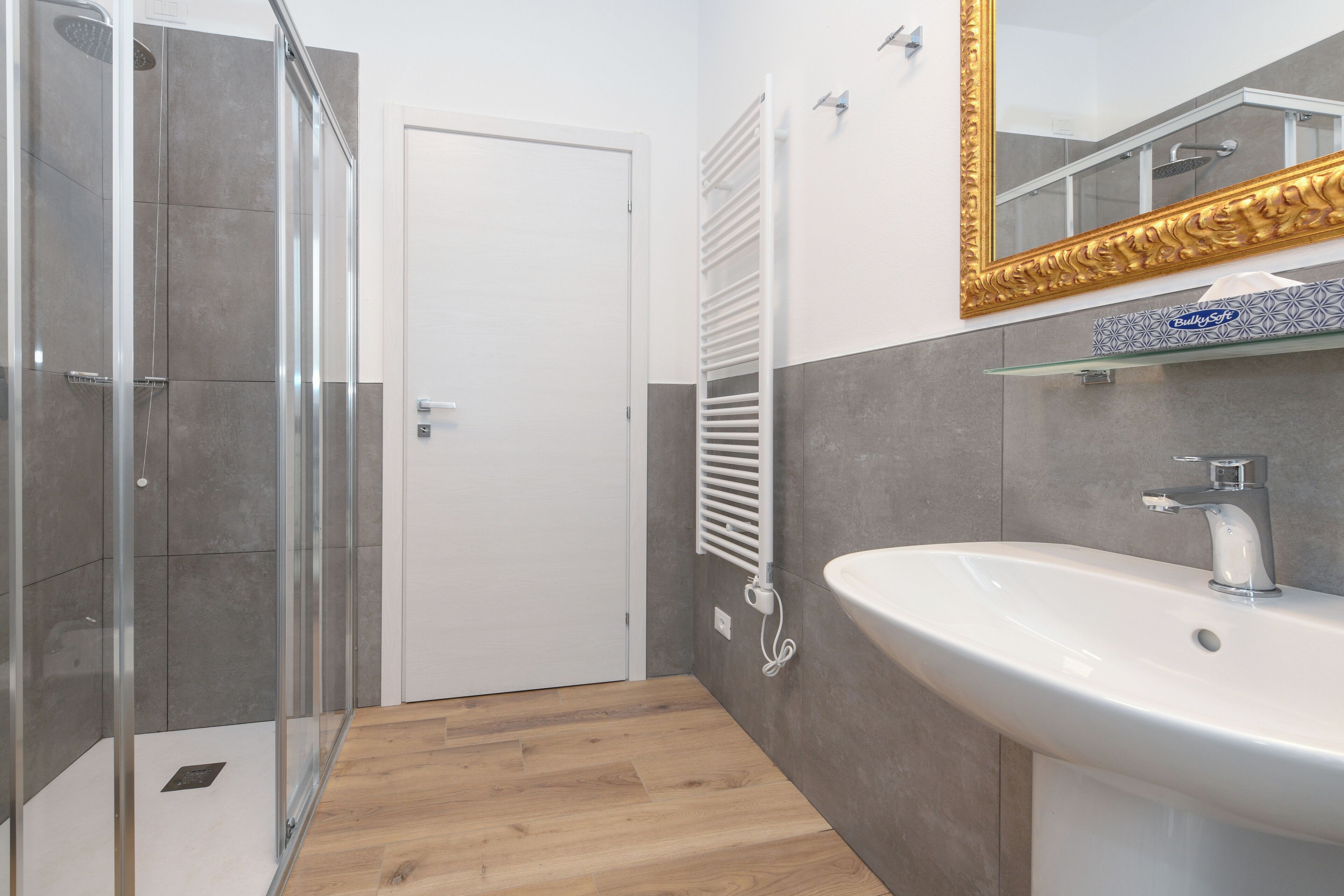 A modern bathroom with a glass shower enclosure, a white sink, and a large mirror with a decorative frame.