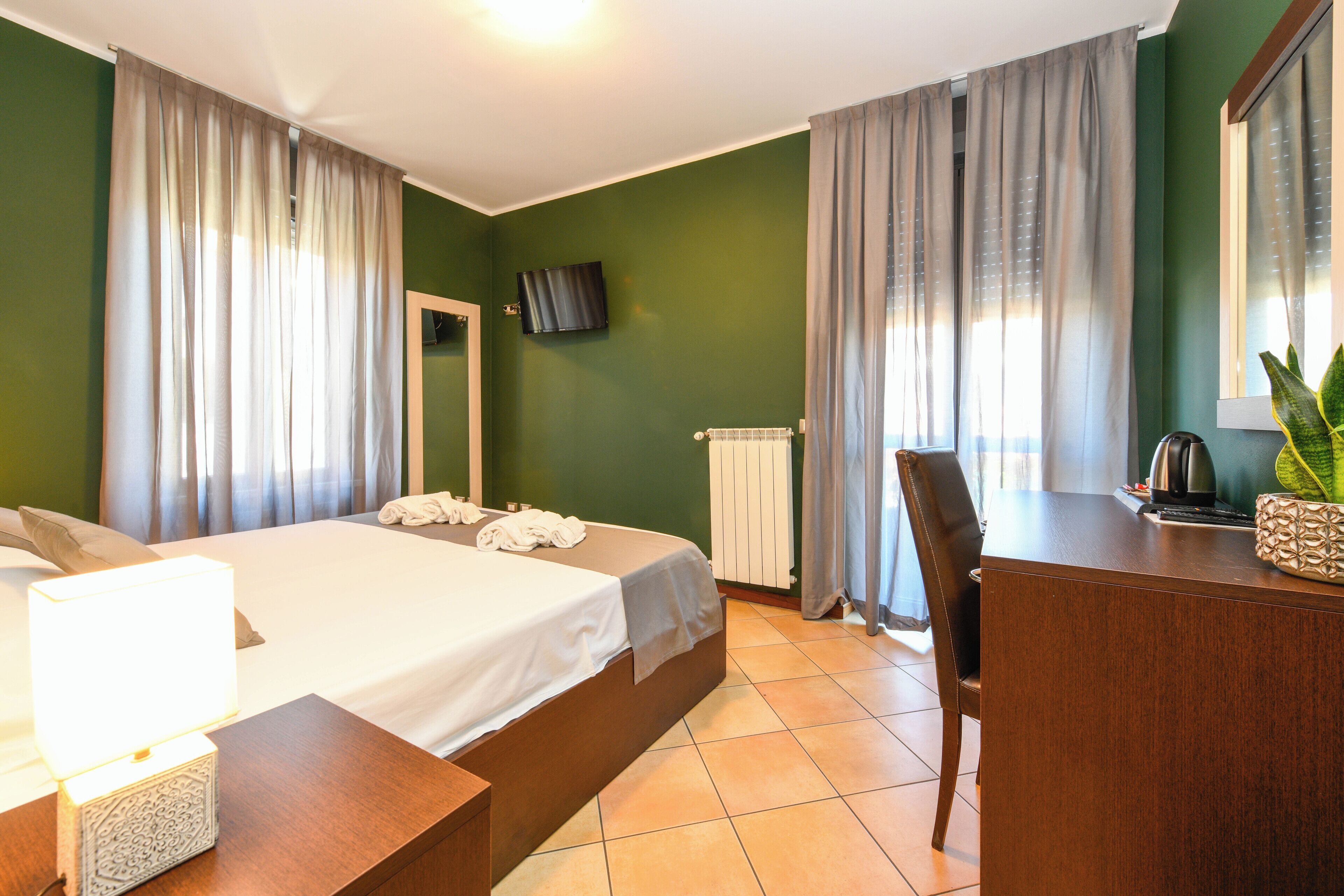 A hotel room with a bed, a desk, a chair, a TV, and a window with curtains.