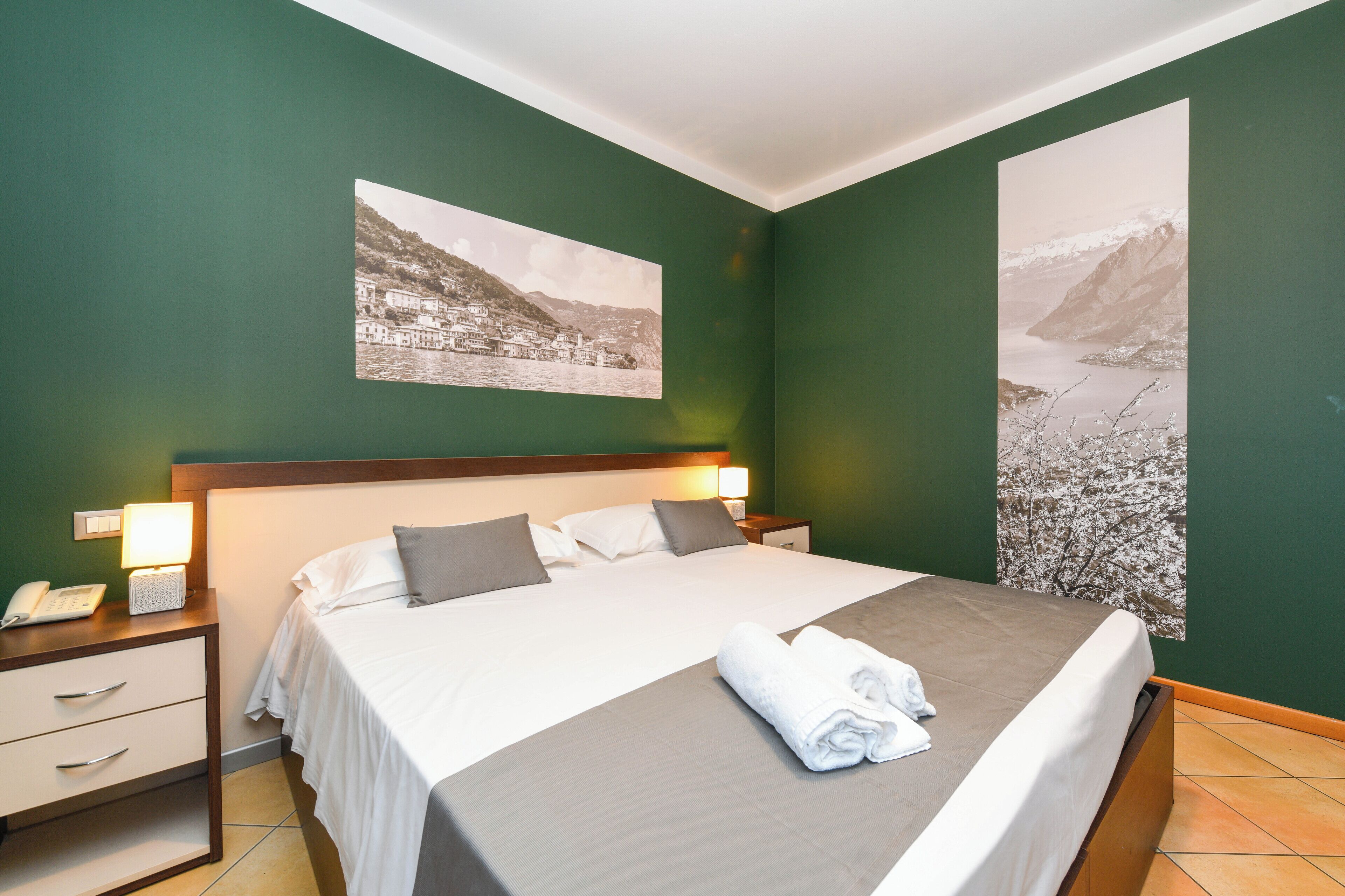 Ein Hotelzimmer mit einem großen Bett, zwei Nachttischen, einer Nachttischlampe, einem Telefon und einem gefalteten Handtuch auf dem Bett.