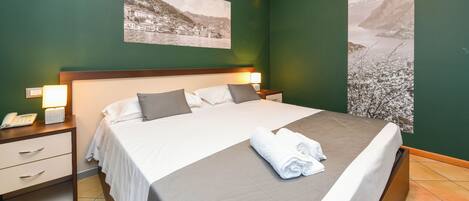 A hotel room with a large bed, two nightstands, a bedside lamp, a phone, and a folded towel on the bed.