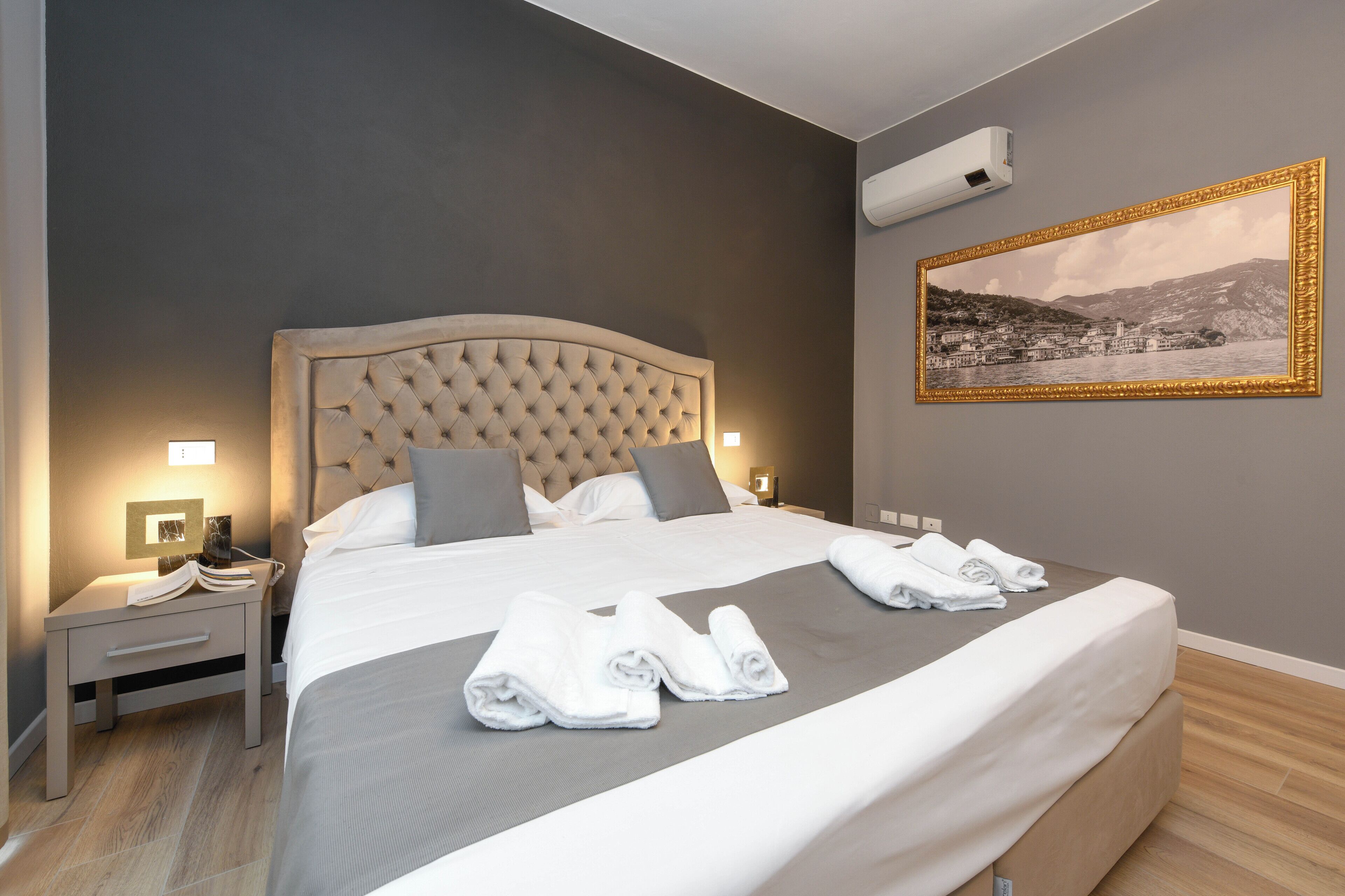 Habitación de hotel con una cama grande, una mesita de noche, aire acondicionado de pared y un cuadro enmarco.