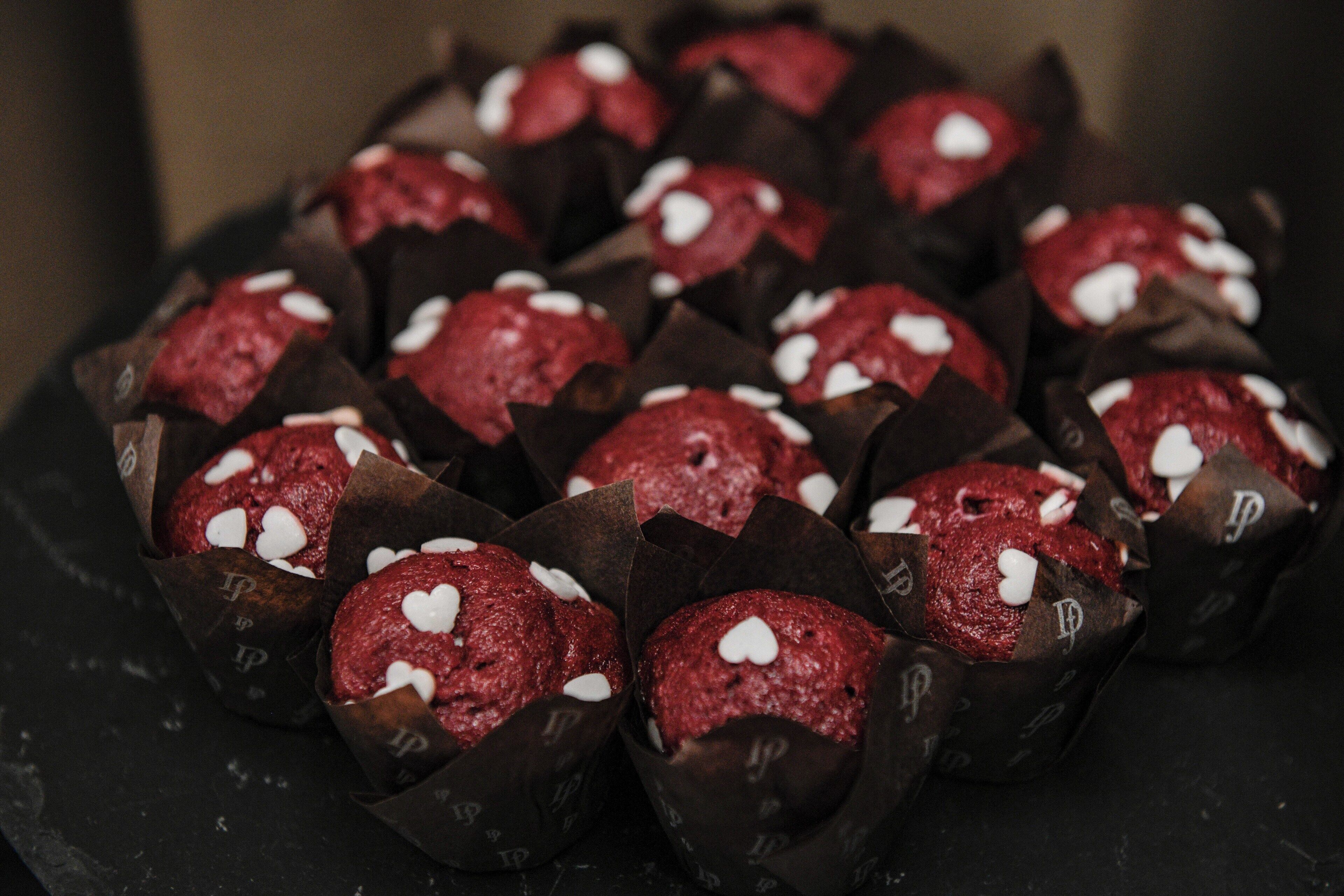 Una bandeja de cupcakes de terciopelo rojo con decoraciones en forma de corazón blanco.