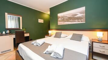 Habitación de hotel con cama, mesitas de noche, escritorio, silla, espejo y un cuadro colgado en la pared.