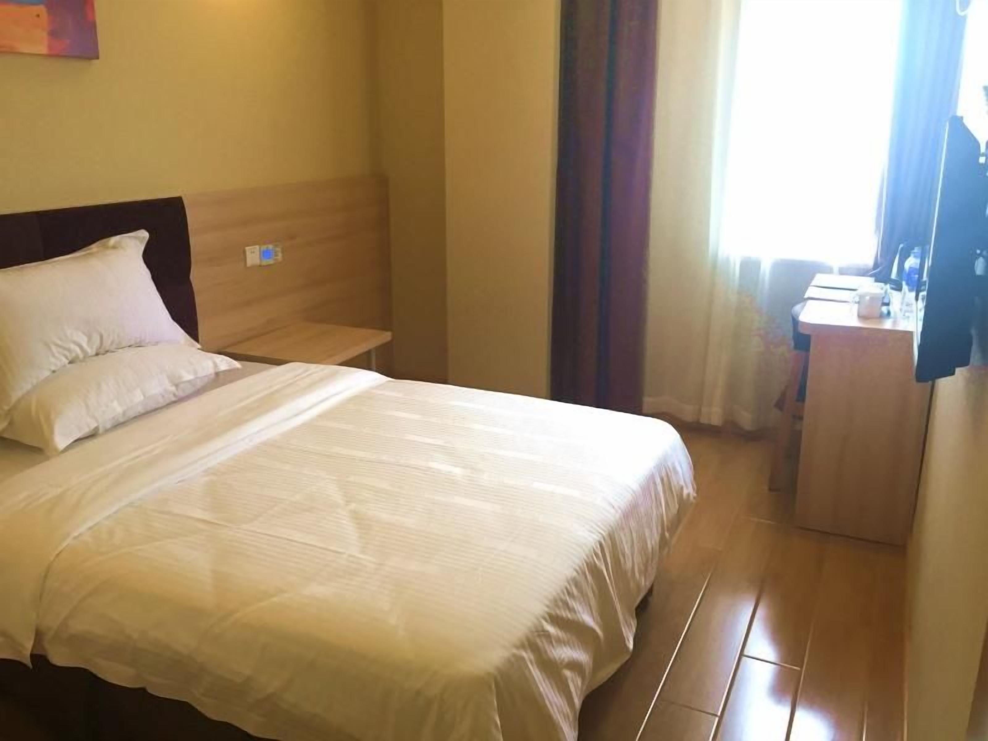 A hotel room with a bed, a bedside table, a desk, and a window with curtains.