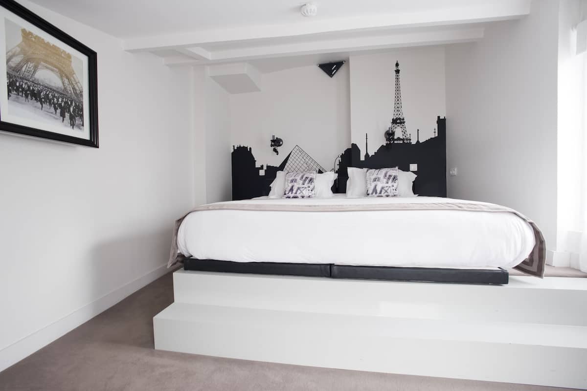 A modern bedroom with a white bed, black headboard, and Eiffel Tower silhouette decor.