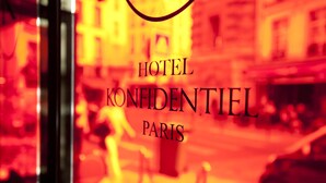 Vista borrosa de una calle con un cartel de 'HOTEL KONFIENTIEL PARIS' en primer plano.