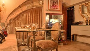 Un comedor con una mesa de vidrio, sillas de terciopelo, una araña y un piano.