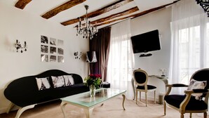 Una sala de estar con un sofá negro, una mesa de centro de vidrio, una silla de madera y un televisor montado en la pared.