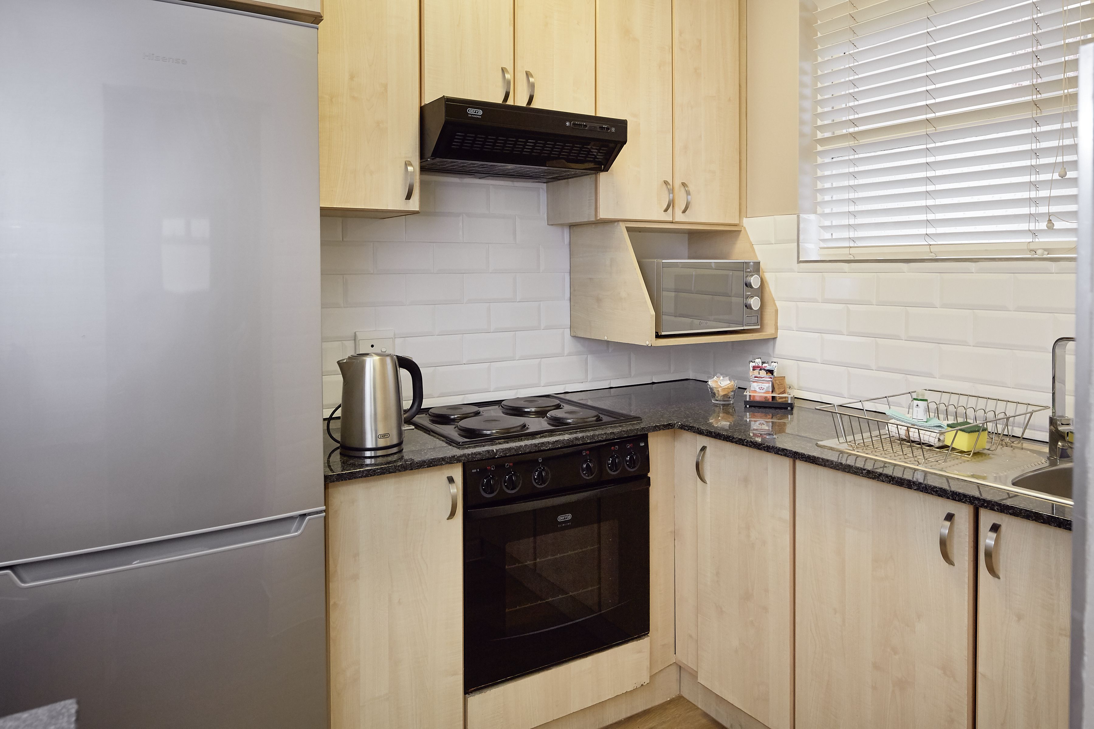 A compact kitchen with a refrigerator, stove, oven, microwave, and wooden cabinets.