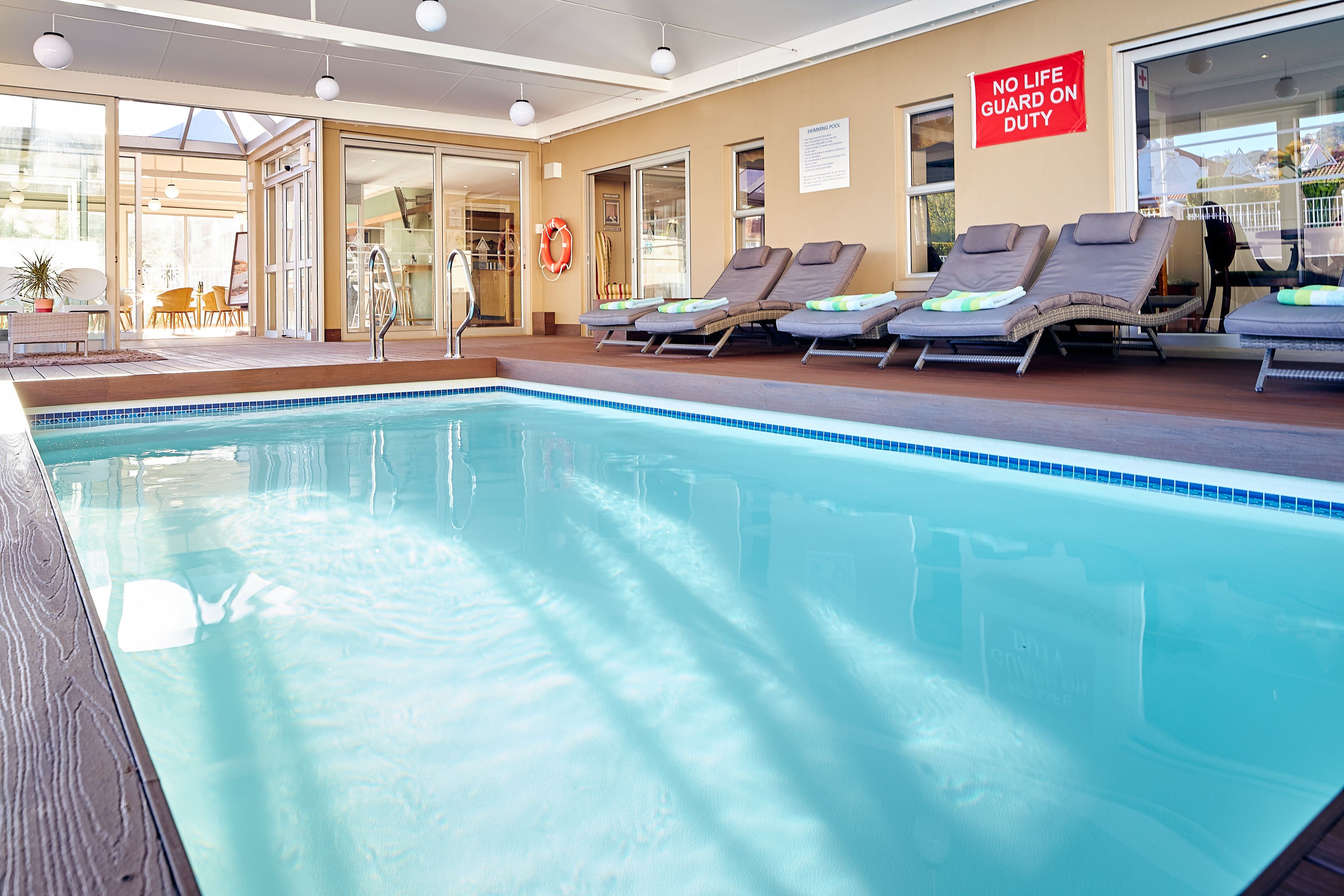 An indoor swimming pool with lounge chairs and a 'No Life Guard on Duty' sign.
