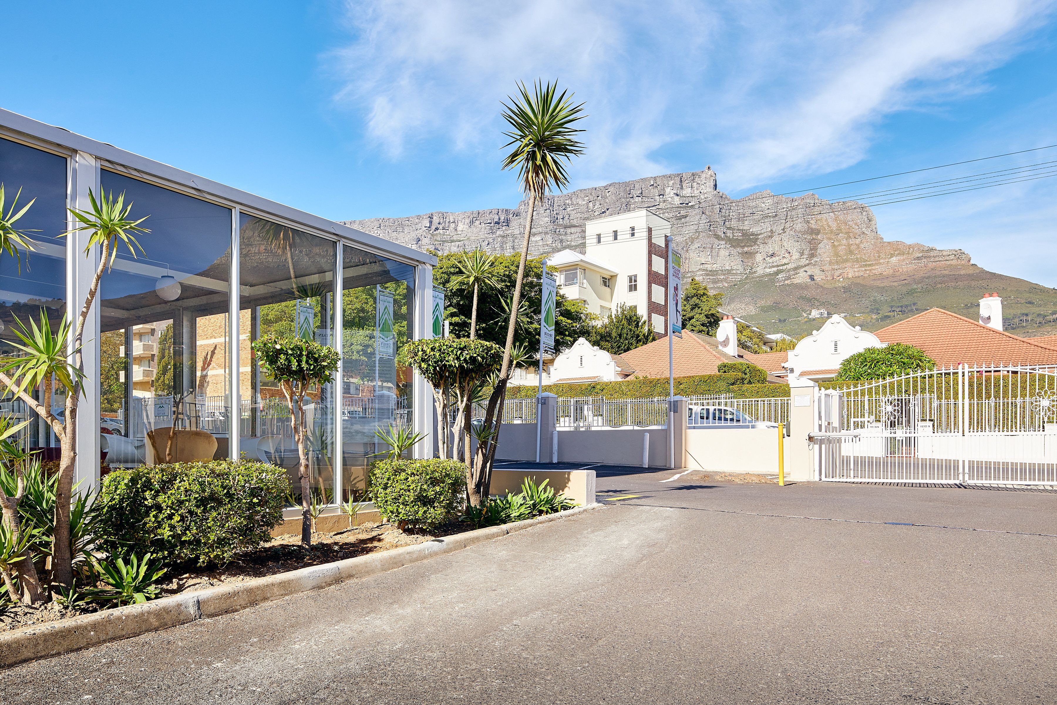 A modern building with large glass windows, a white fence, and a mountain in the background.