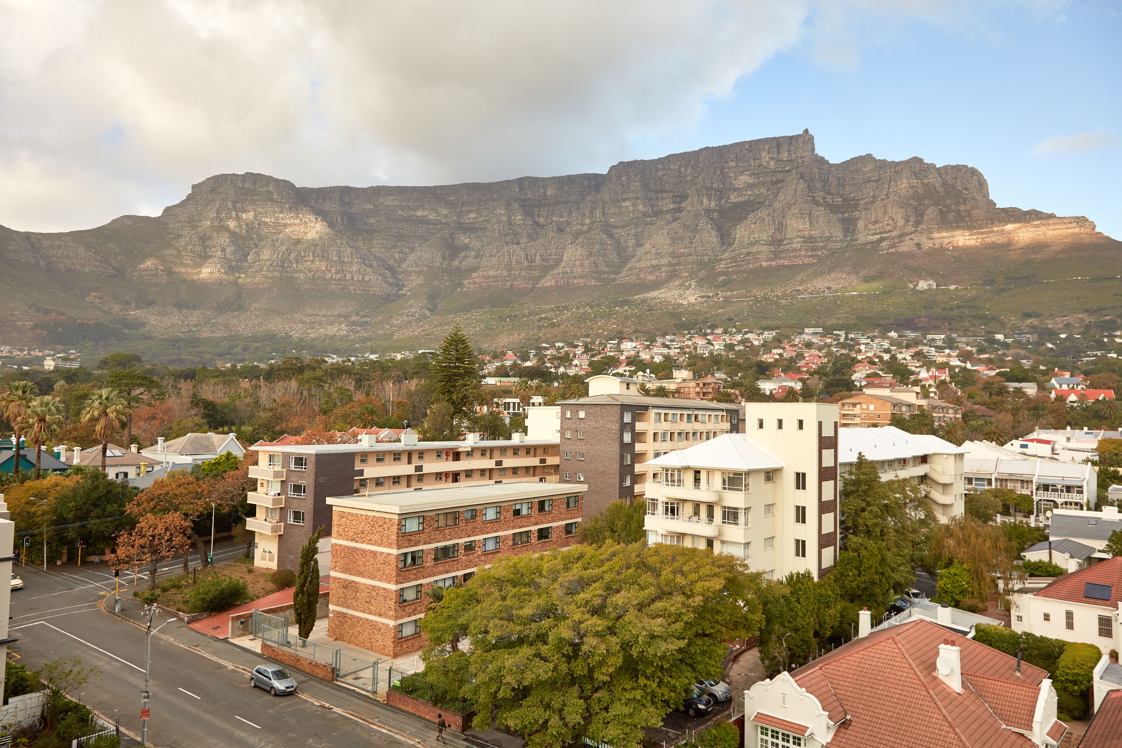 A cityscape with a prominent mountain in the background, residential buildings, and a road with vehicles.