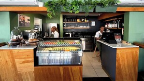 Una cafetería con una máquina de café, un mostrador refrigerado y un cartel de pago sin efectivo.