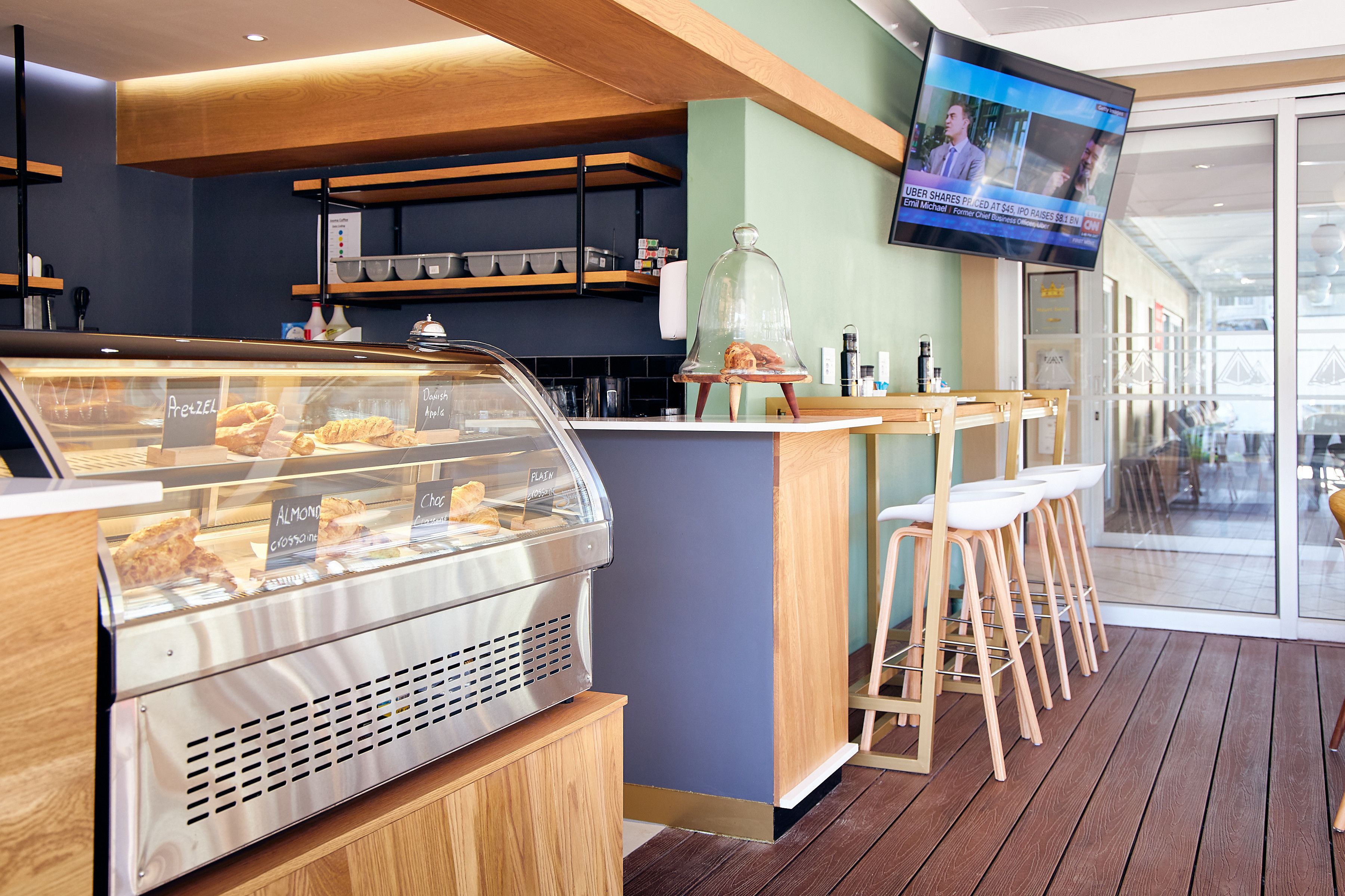 A bakery counter with a display case of pastries, a television screen, and a wooden bar area with stools.