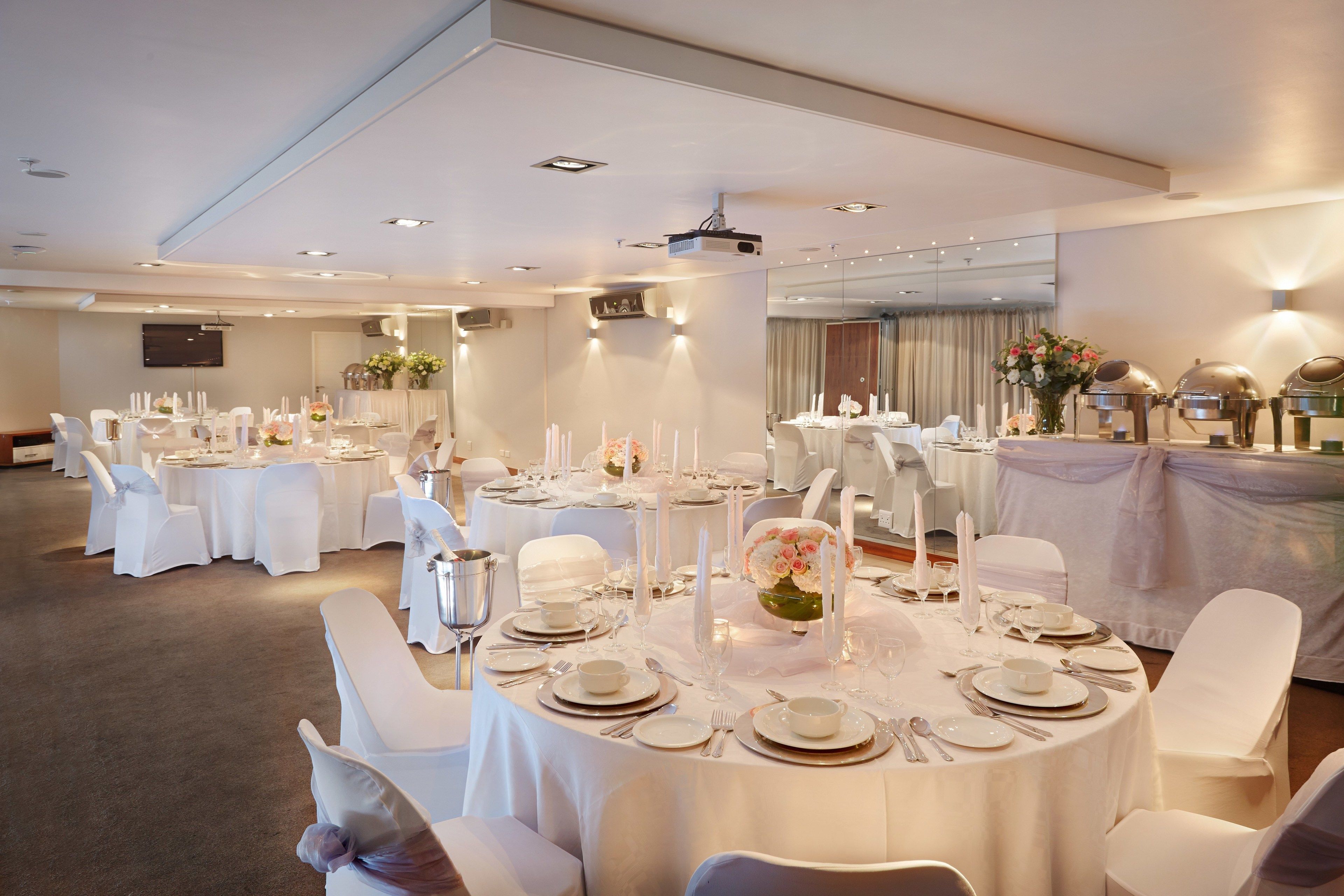 A banquet hall with round tables set for a formal event, featuring white tablecloths, chairs, and floral centerpieces.