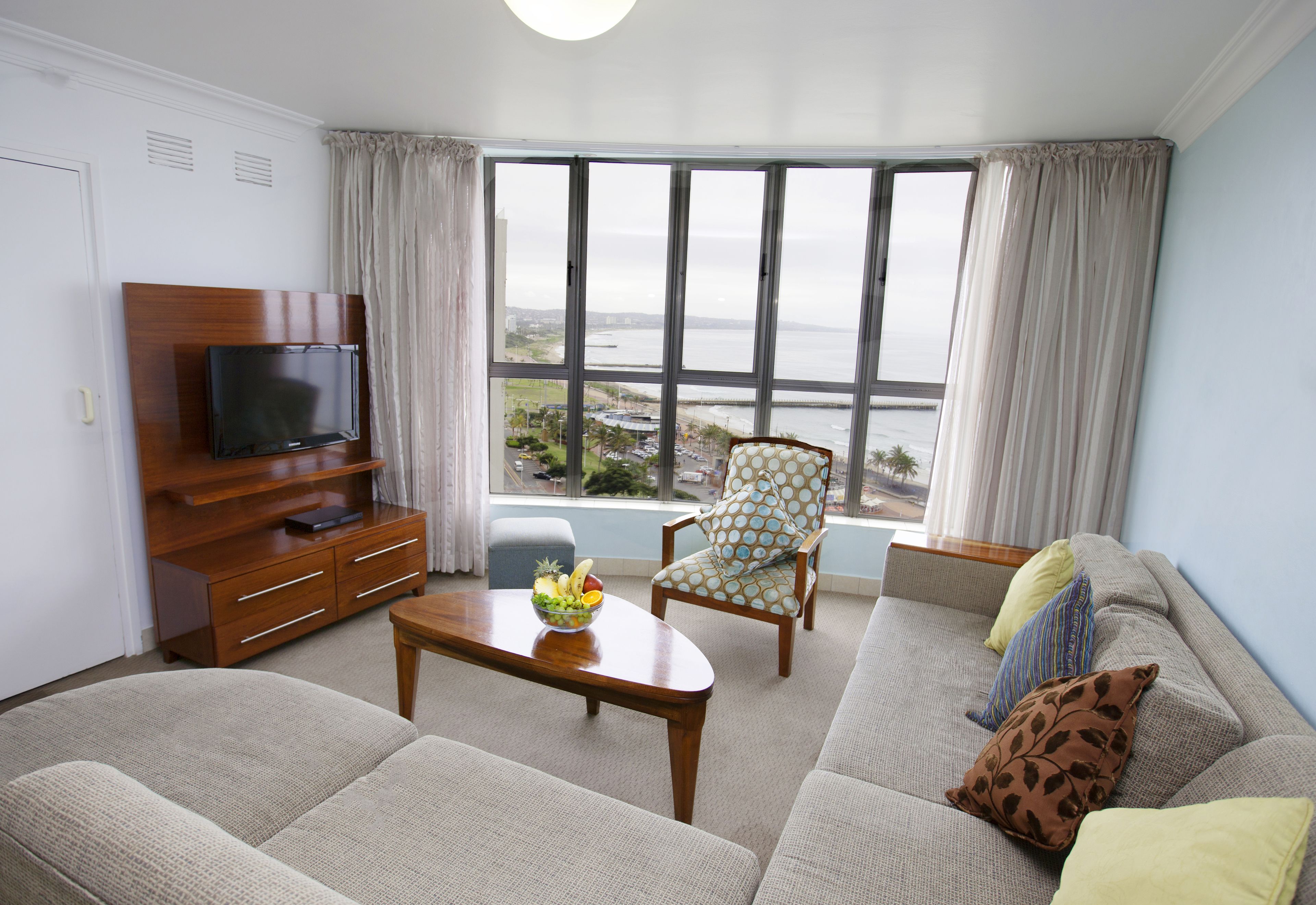 Una sala de estar con sofá, sillón, televisión y una mesa con frutero.