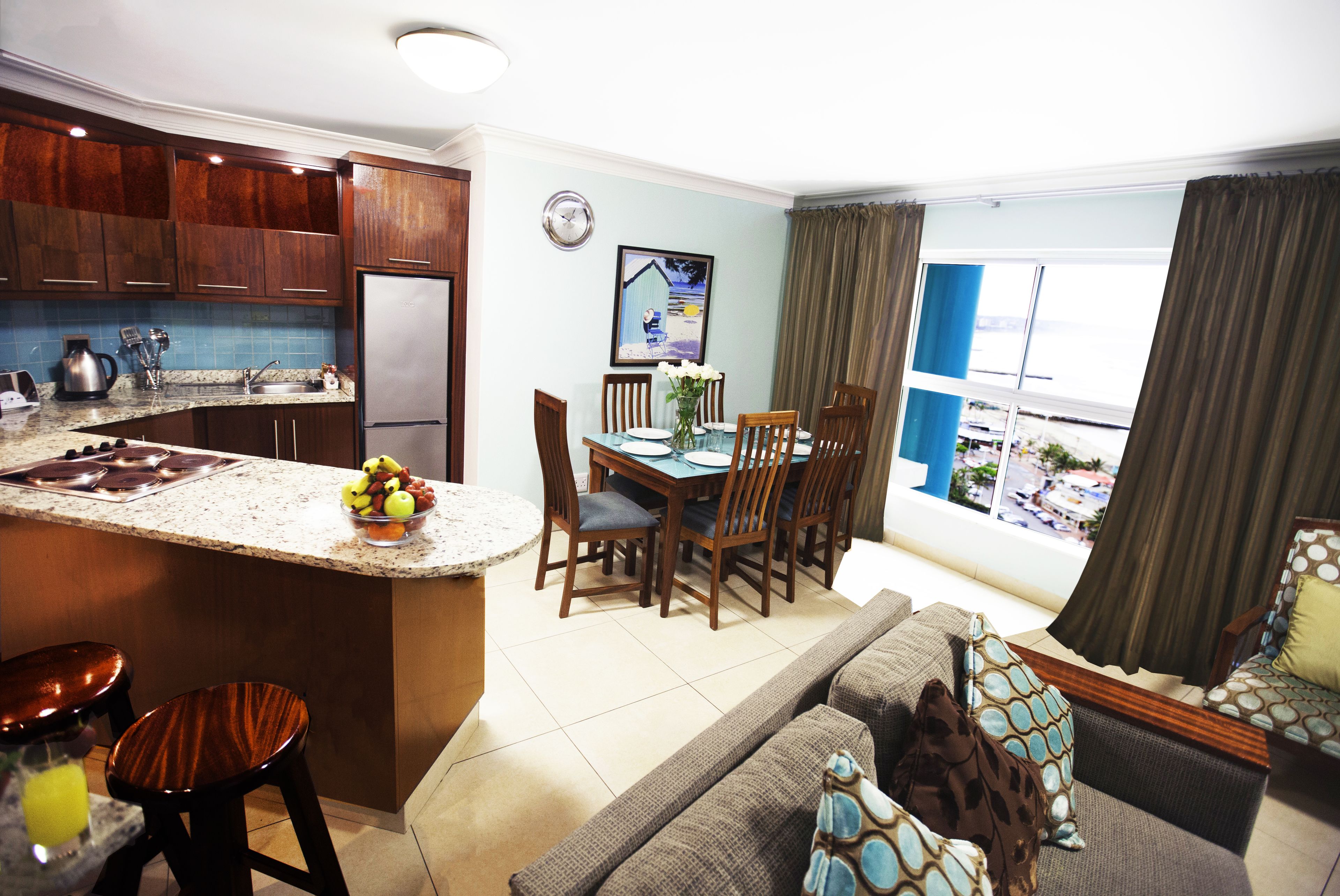 A modern kitchen with a central island, dining area with chairs, and a sofa with patterned cushions.