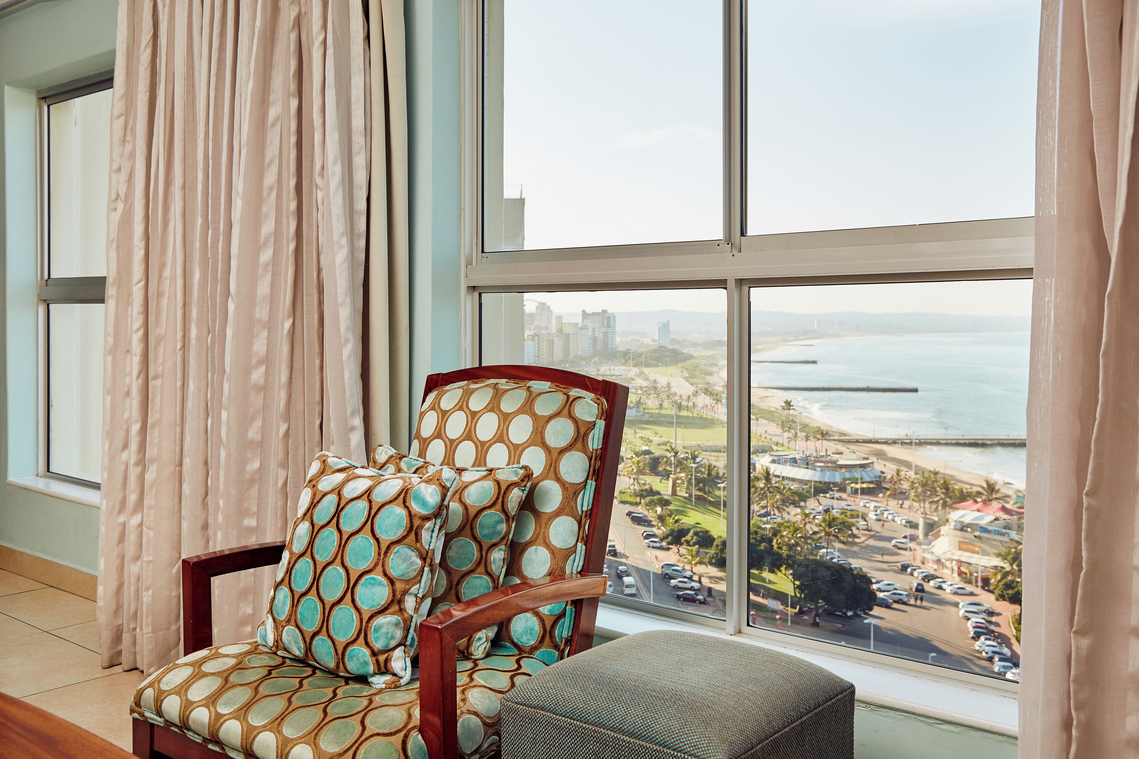 A room with a large window, a patterned armchair, and a view of a coastal area.