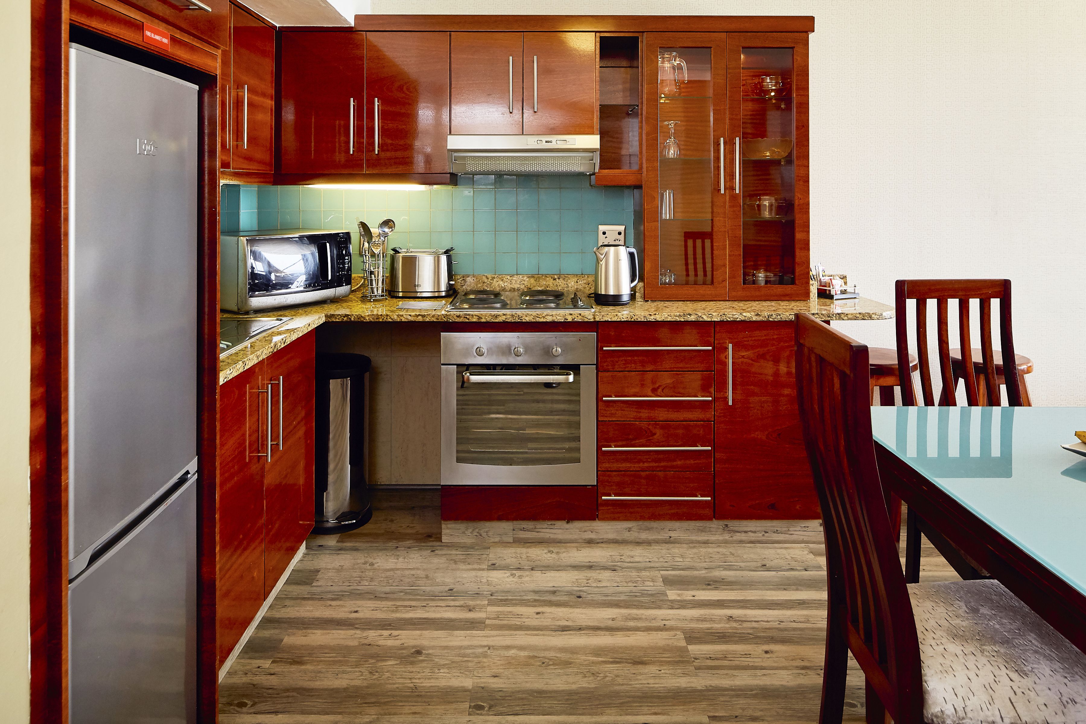 Una cocina con armarios de madera, un refrigerador de acero inoxidable, un microondas, un horno y una mesa de comedor con sillas.