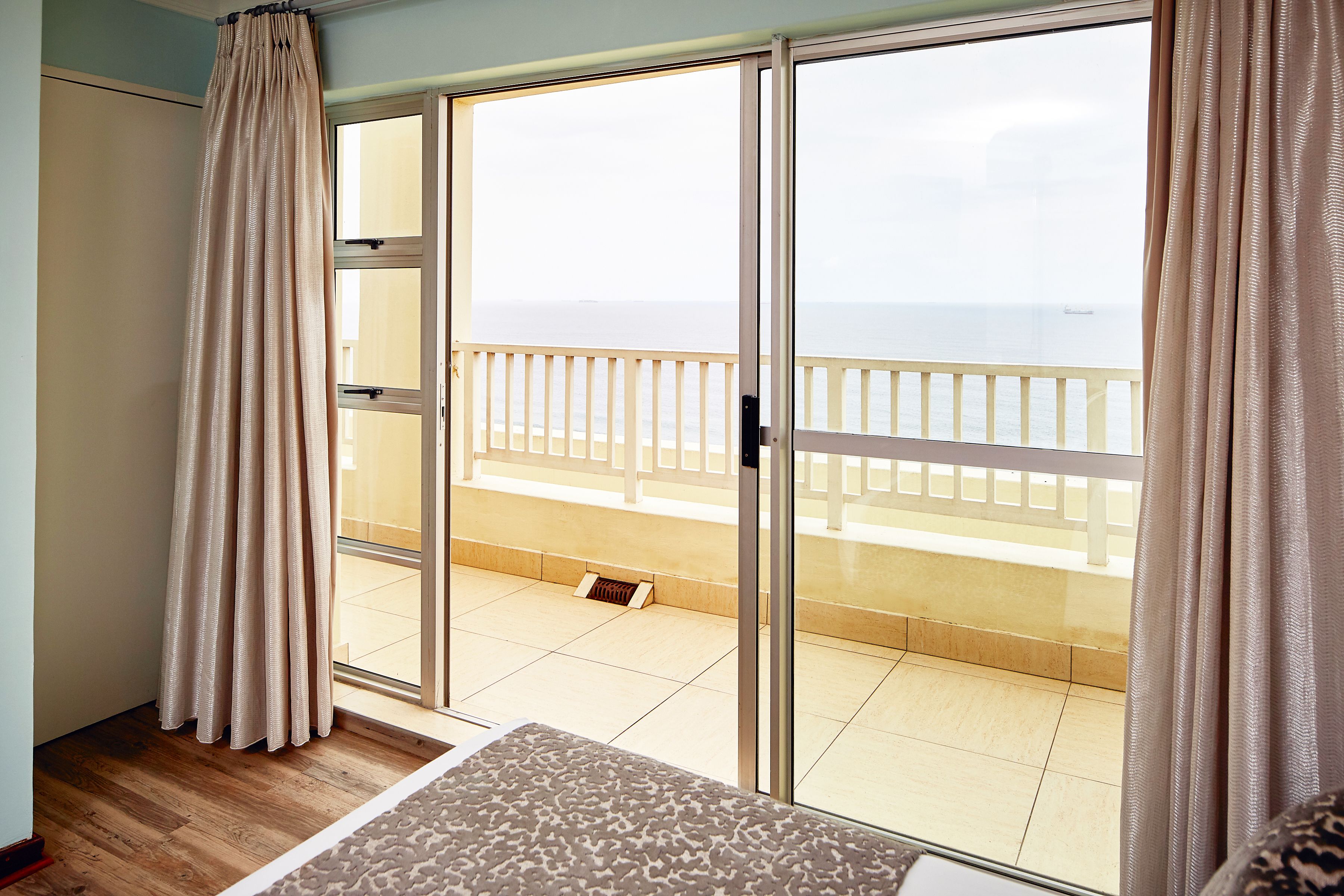 A room with a large sliding glass door leading to a balcony with a view of the sea.