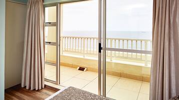 A room with a large sliding glass door leading to a balcony with a view of the sea.
